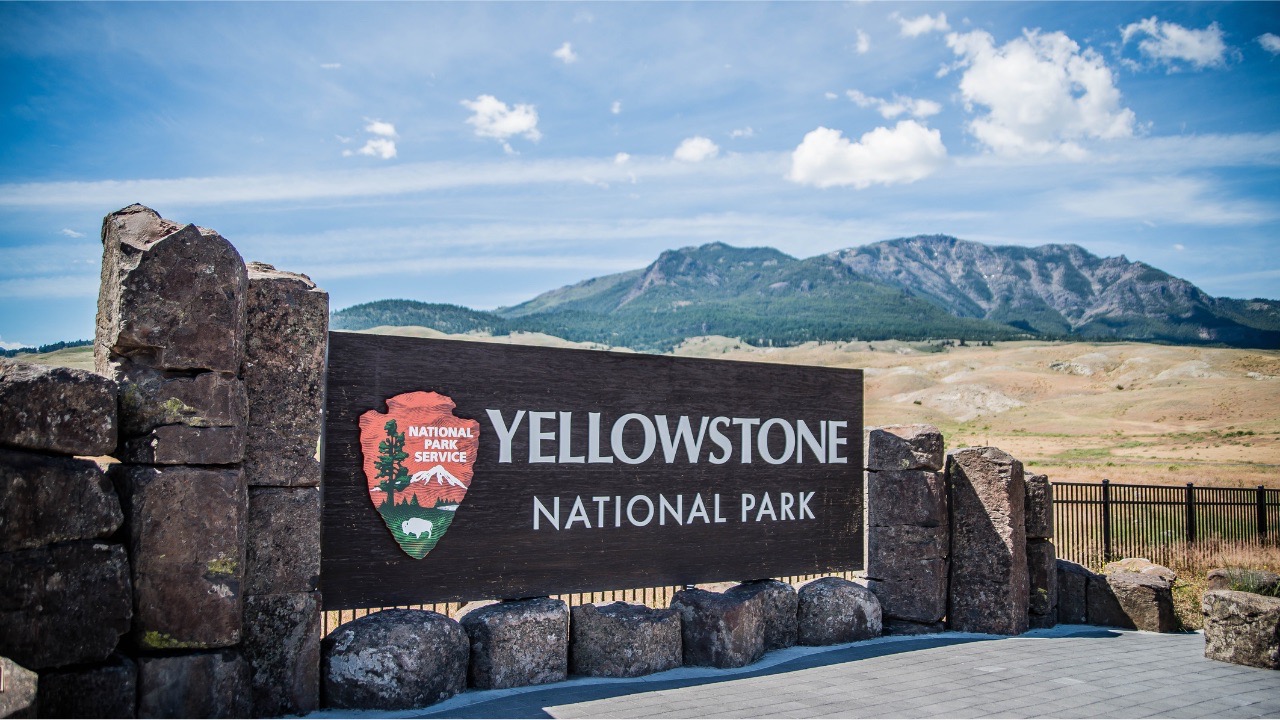 Yellowstone National Park entrance sign with mountains behind it