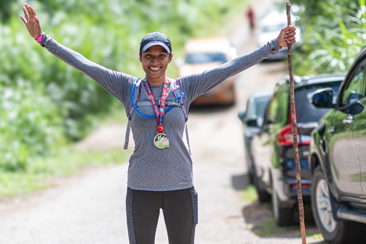 A smiling finisher with her arms raised and a medal around her neck
