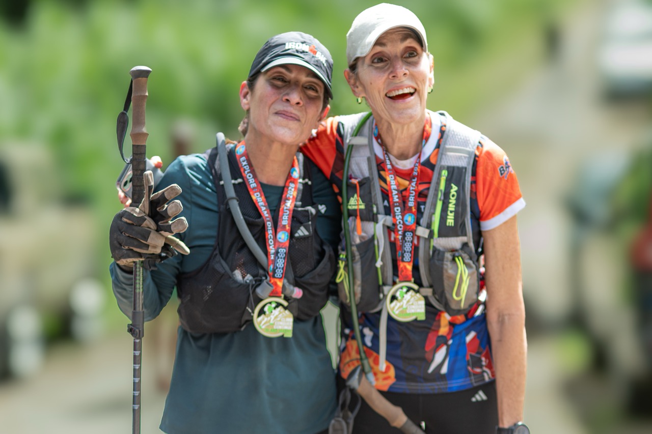 Two women finishers with trekking poles and medals