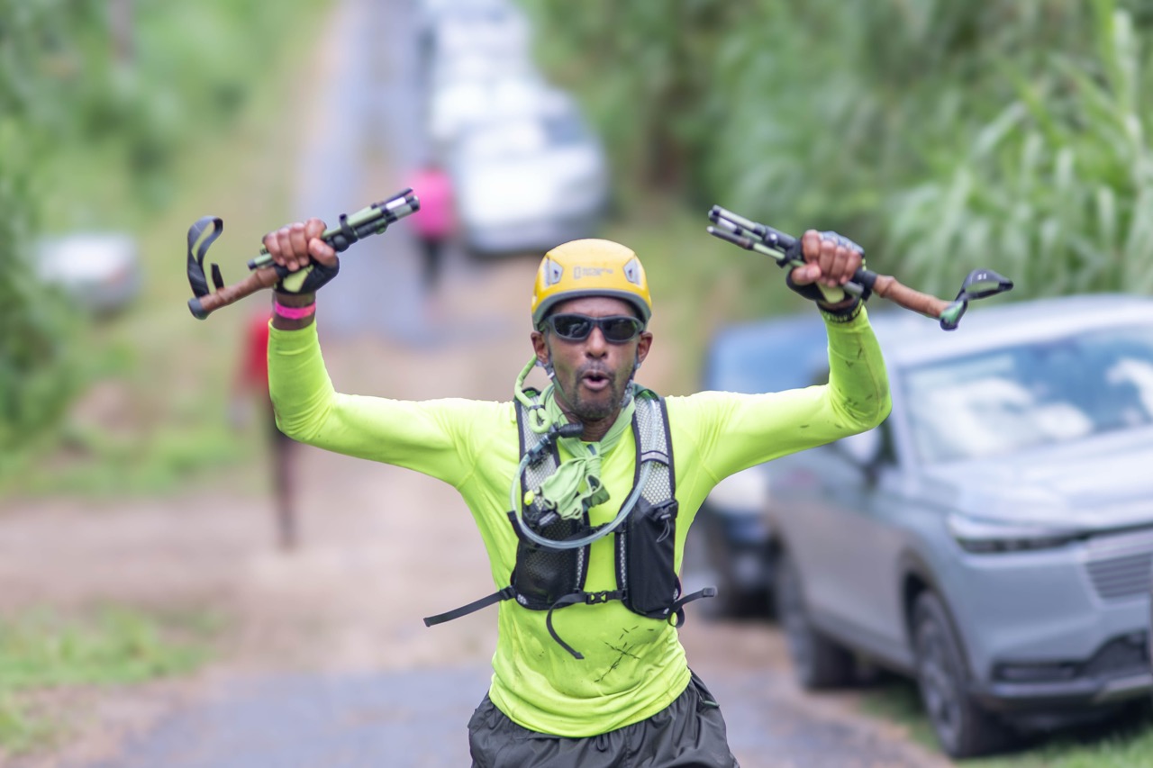 A hiker in a yellow helmet raising his trekking poles